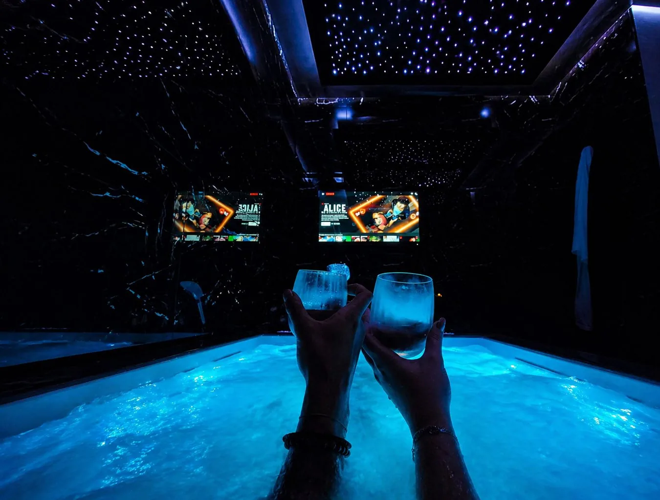 Deux personnes trinquent dans le jacuzzi privatif sous le ciel étoilé de La Duchesse 1976